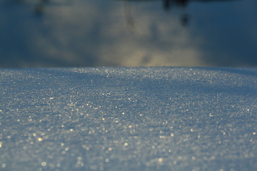 Blue snow sparkling in the setting sun. Shadows on the blue shining snow. Shining snowy surface on a winter evening.