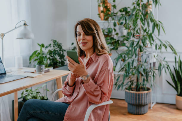 istock Working from Home: a Beautiful Happy Senior Woman Using her Smartphone at her Home Office 1305535929