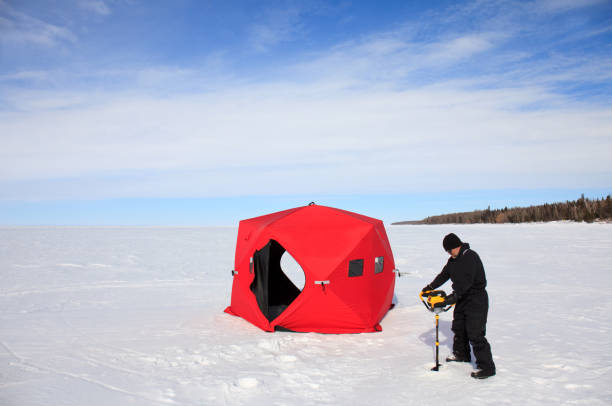 Man Drilling Hole In Ice With Auger For Ice Fishing In Manitoba Canada A caucasian male drilling a hole with an ice auger for ice fishing expedition in Manitoba, Canada. A red collapsible ice fishing shelter is also in the image. man ice fishing stock pictures, royalty-free photos & images