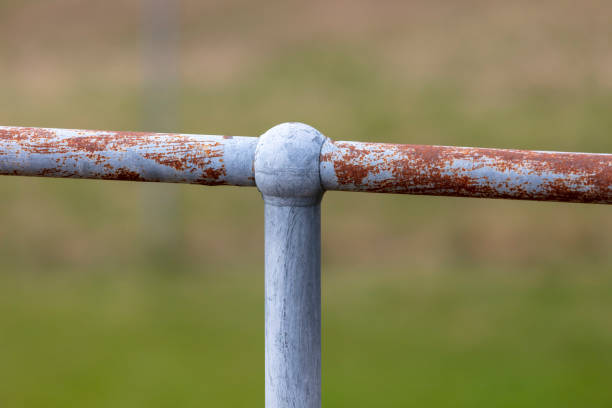 A rusty steel galvanised fence post and hand rail on a green grass background
