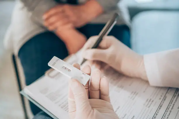 Close-up shot of doctor's hand with protective gloves holding a positive test device to senior patient. Doctor documented the result after a positive test. Doctor hand holding positive Coronavirus/Covid-19 rapid test.