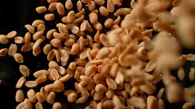 SLO MO LD Roasted peanuts falling onto black surface