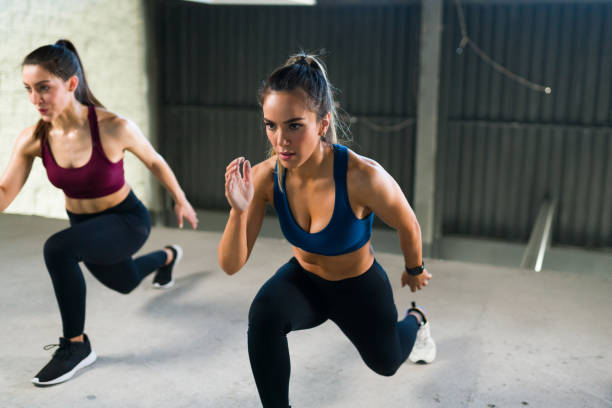 Fit hispanic woman in activewear exercising at the gym Athletic young woman with a healthy lifestyle doing leg lunges during a HIIT class. Women working out together at the fitness center exercise class stock pictures, royalty-free photos & images
