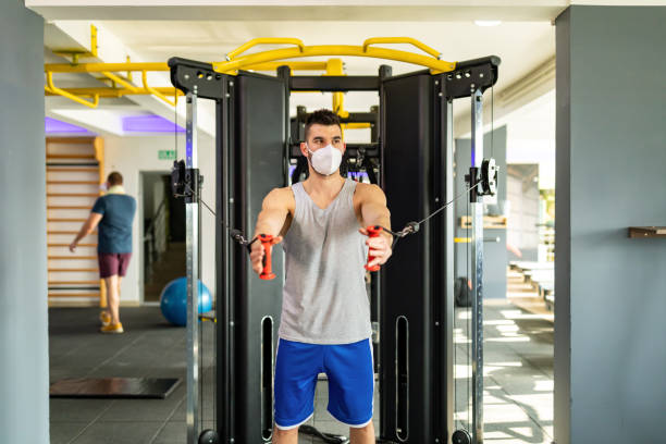 istock Man doing strength workout exercise in gym with face mask 1305550470
