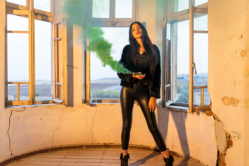 Female figure celebrating with green smoke bomb standing among illuminated smoke cloud