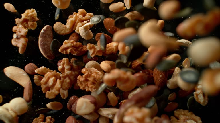 SLO MO LD Mix of nuts and seeds falling onto black surface