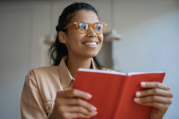Beautiful smiling woman reading book, working, sitting at home Beautiful smiling woman reading book, working, sitting at home. Portrait of happy student in stylish eyeglasses studying, learning language, exam preparation, education concept reading glasses stock pictures, royalty-free photos & images