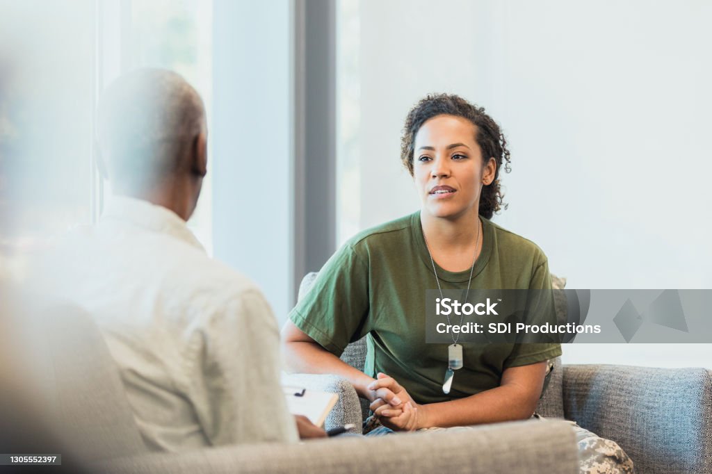 Female soldier talking with mental health professional A serious mid adult female soldier talks to a male mental health professional about hard situations while serving overseas. Veteran Stock Photo