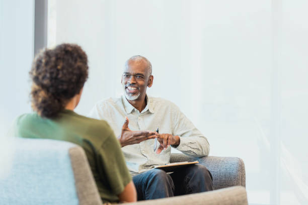 Unrecognizable woman listens as cheerful counselor gestures and speaks An unrecognizable mid adult woman listens as the cheerful mature adult male counselor gestures and speaks. psychotherapy stock pictures, royalty-free photos & images