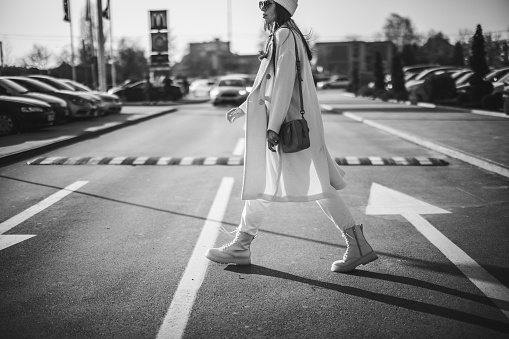 Young stylish woman with cap and sunglasses walking across street