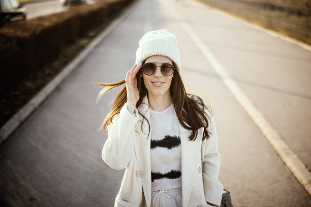 istock Young woman with sunglasses walking on sidewalk on sunny day 1305555320