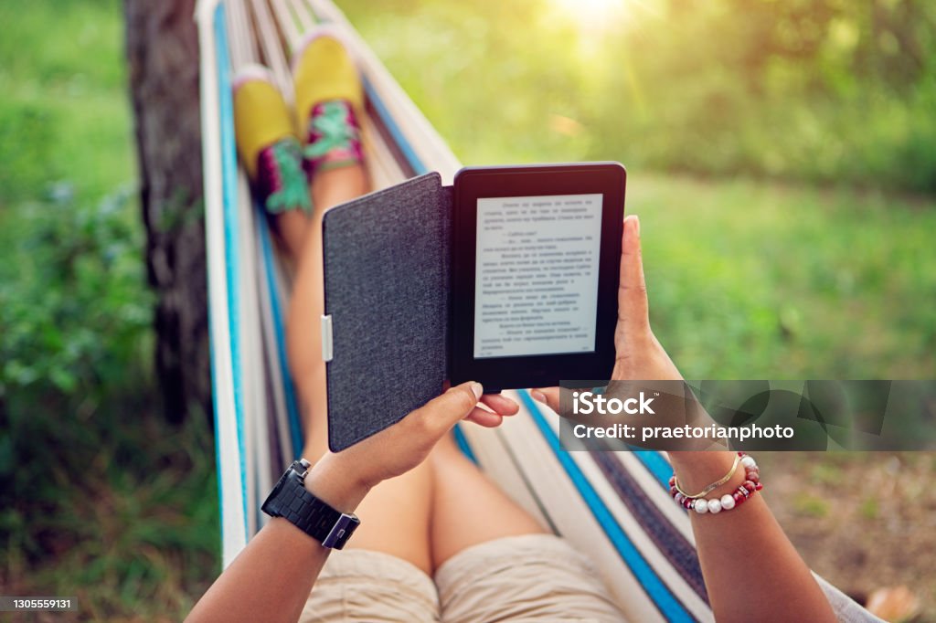 Woman is reading e-book in a hammock Woman is reading e-book in a hammock /focus point is on the e-book/ E-Reader Stock Photo