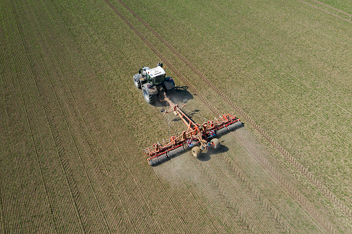 Aerial view of an agricultural tractor with high speed stubble cultivator harrow working in field in spring.