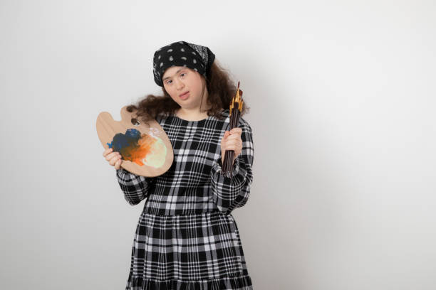 istock Adorable young girl with down syndrome holding painter palette 1305561199