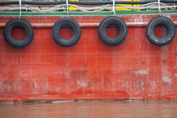 Side view of a tug boat with rubber tires hanging on its red steel exterior haul