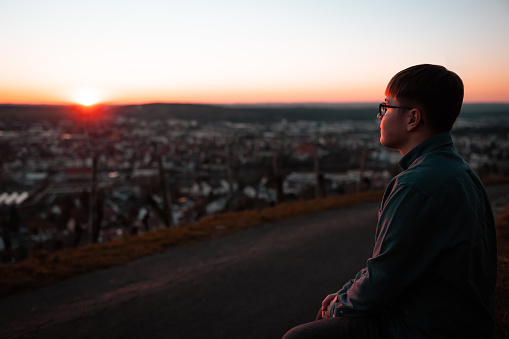 Pensive young teenage man standing alone on hill top looking over into the sunset. Enjoying the view and tranquility of the setting sun. Millennial Generation Moody Tranquil Outdoor Portrait.