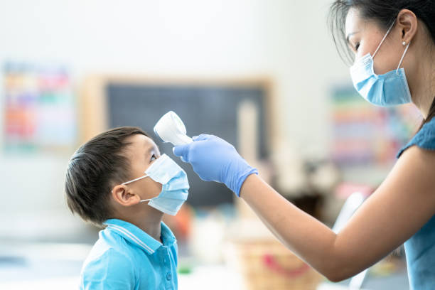 istock Teacher Checking Student's Temperature In A Classroom Stock Photo 1305568232