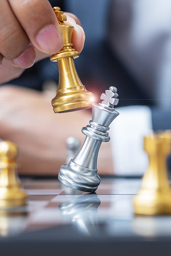 businessman hand moving gold Chess King figure and Checkmate opponent during chessboard competition. Strategy, Success, management, business planning, disruption and leadership concept