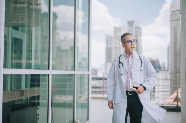 asian chinese male doctor walking towards his office - senior adult hospital uniform gray hair imagens e fotografias de stock