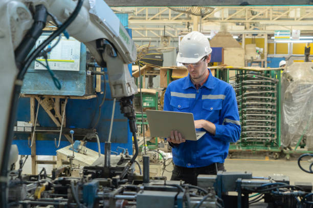istock Western man, caucasian, an engineer or worker use laptop notebook computer device to control smart robot welding hand system automate manufacturing machine engine in factory, industry. People 1305592775