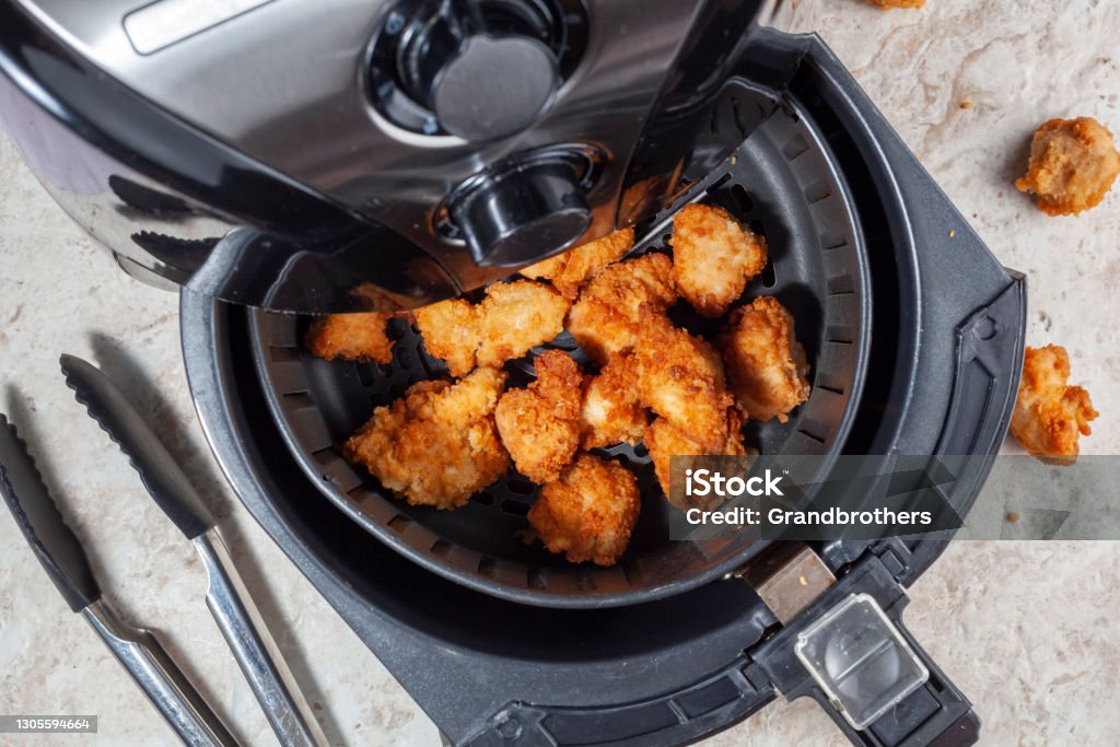 Air frying homemade chicken nuggets Close up flat lay image of an air fryer oven on kitchen countertop. This offers fast and easy crispy food with little or no fat by circulating hot air inside the basket. A healthy snack alternative. Air Fryer Stock Photo