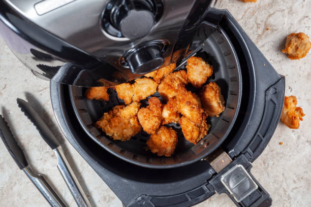 Air frying homemade chicken nuggets Close up flat lay image of an air fryer oven on kitchen countertop. This offers fast and easy crispy food with little or no fat by circulating hot air inside the basket. A healthy snack alternative. nuggets heat stock pictures, royalty-free photos & images