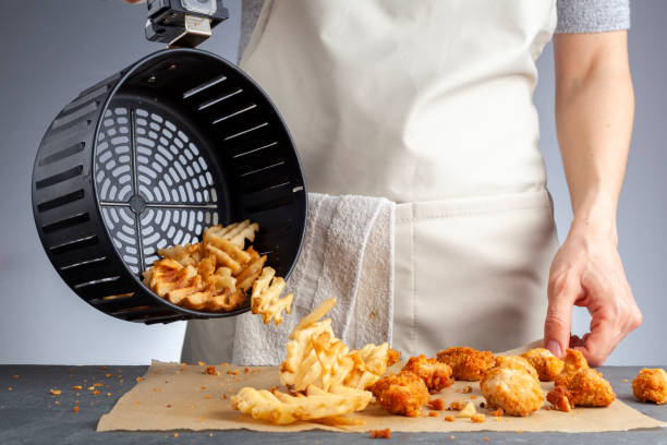 Air frying waffle potato fries at home A woman is dumping fresh made potato waffle fries from basket onto a countertop together with chicken nuggets. She fried them in air fryer using very little fat. A healthy homemade convenient snack. nuggets heat stock pictures, royalty-free photos & images