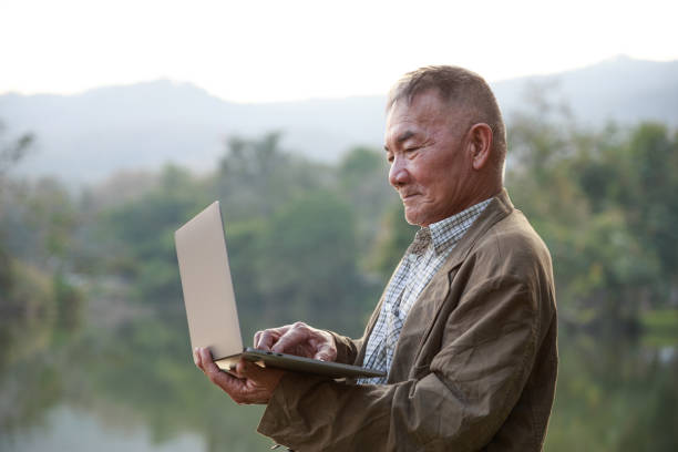istock Asian old man using laptop in public park. 1305597813