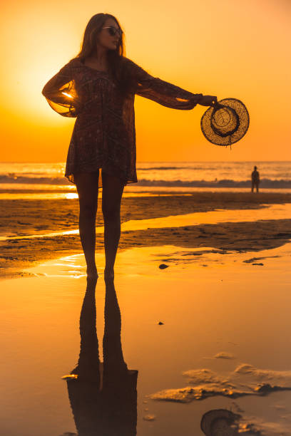 istock Lifestyle, a young blonde with a hat reflected in a sunset on the beach 1305602875