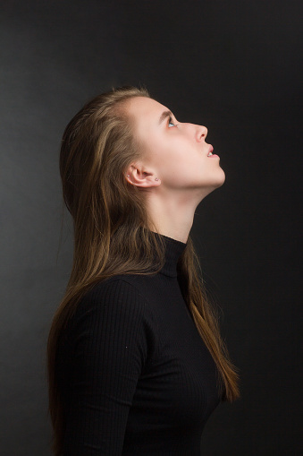 portrait of a young beautiful woman in a studio in dark colors. looks up, turned in profile