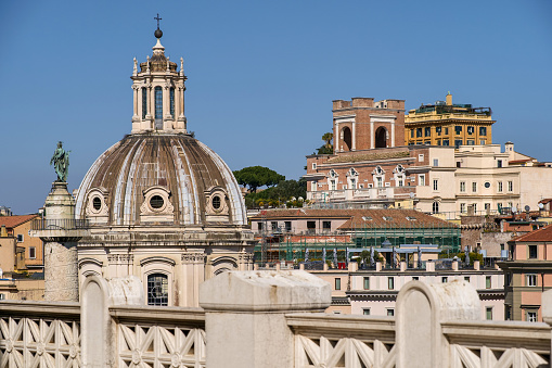 The horizon over the rooftops of the historic center of Rome from the panoramic terrace of the Altare della Patria National Monument, in the heart of the Eternal City. In the foreground the dome of the church of the Santissimo Nome di Maria al Foro and the Trajan's column (left). In the background (center) the Presidential House of the Quirinal Palace with the Italian Flag. Image in high definition format.