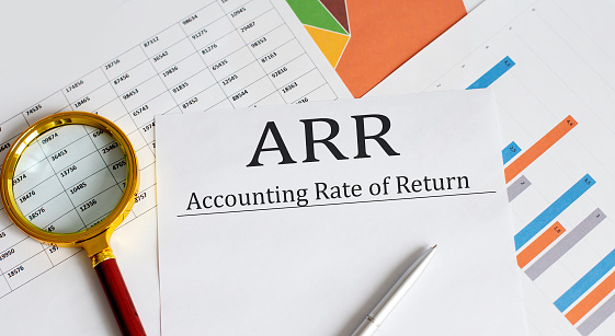 Paper with ARR ACCOUNTING RATE OF RETURN on table with charts, pen and magnifier