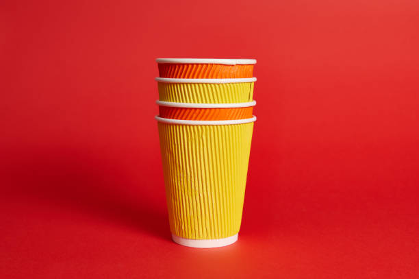 istock Stack of multicolored paper disposable cups for hot drinks on a red background with copy space. 1305608530