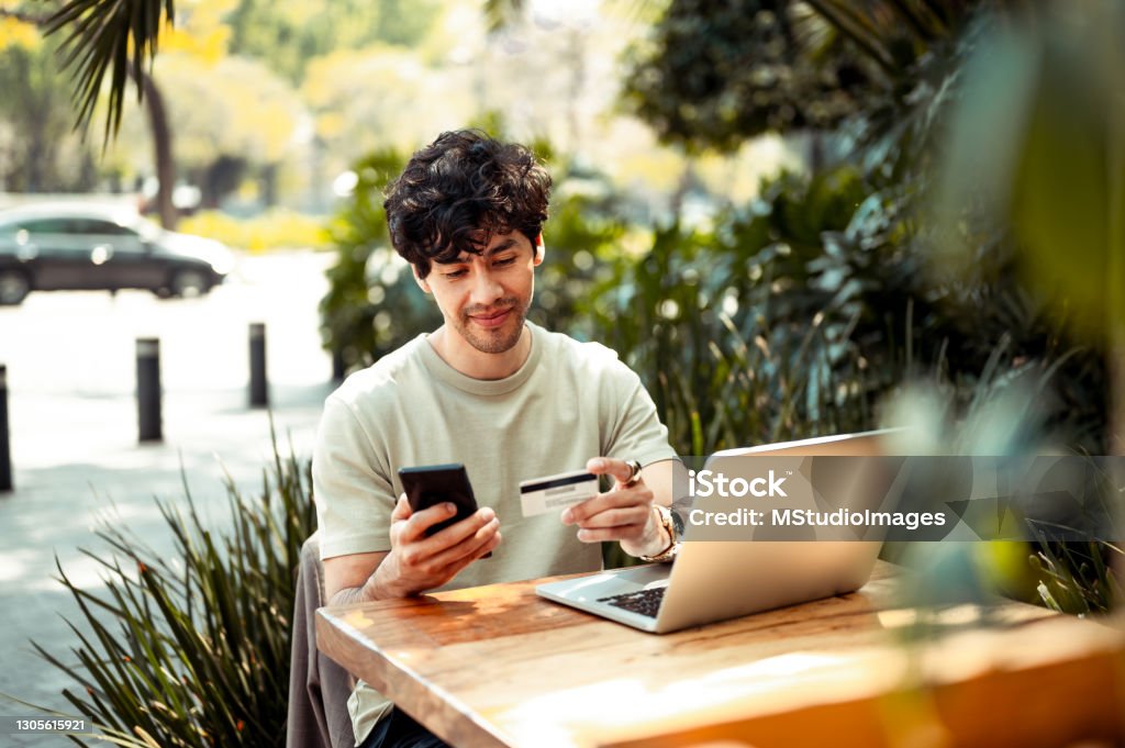 Young man shopping online Young man sitting at the cafe and paying online with credit card Credit Card Stock Photo