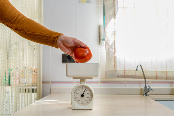 istock Man's hand placing a large red tomato on a scale in the kitchen at home 1305621004