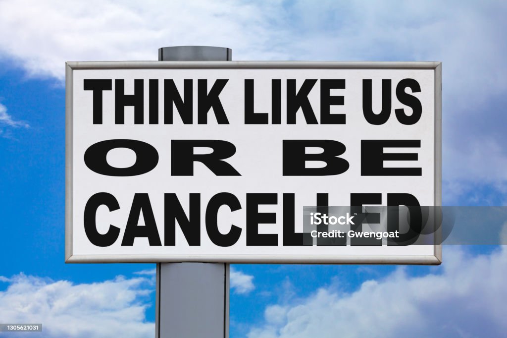 Think like us or be cancelled - Billboard Close-up on a white billboard against a blue sky with the message "Think like us or be cancelled" written in black in the middle. Cancel Culture Stock Photo