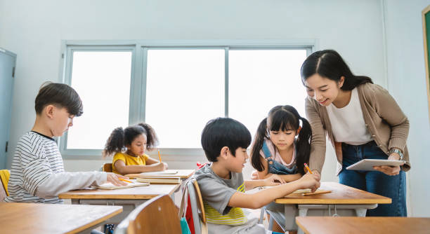 Pupil boy hi five with teacher in classroom at elementary school. Student boy studying in primary school. Children writing notes in classroom. Education knowledge, successful teamwork concept