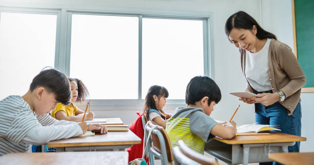 istock Pupil boy hi five with teacher in classroom at elementary school. Student boy studying in primary school. Children writing notes in classroom. Education knowledge, successful teamwork concept banner 1305622365