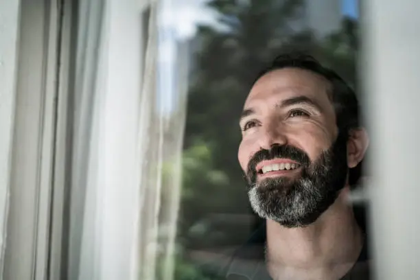 Photo of Mature man looking through window at home