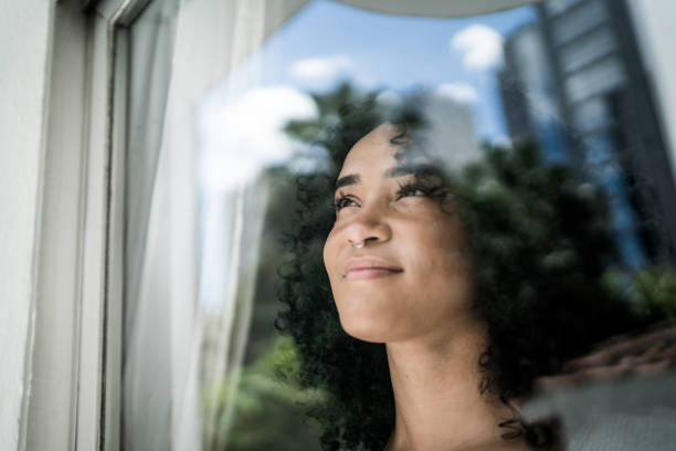 jonge vrouw die door venster thuis kijkt - woman thinking stockfoto's en -beelden