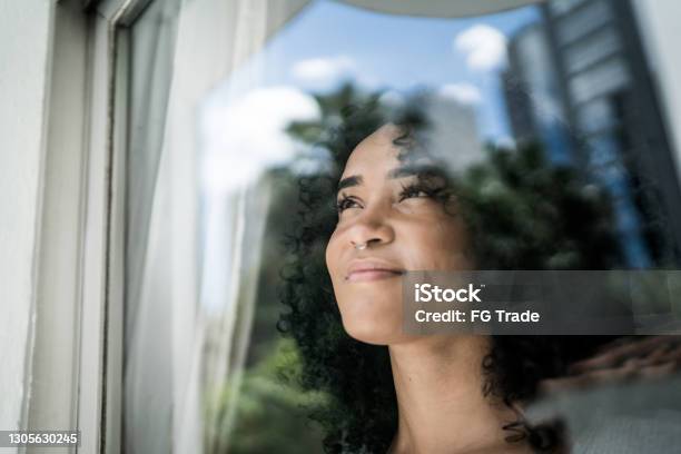 Young Woman Looking Through Window At Home Stock Photo - Download Image Now - Contemplation, Hope - Concept, One Woman Only