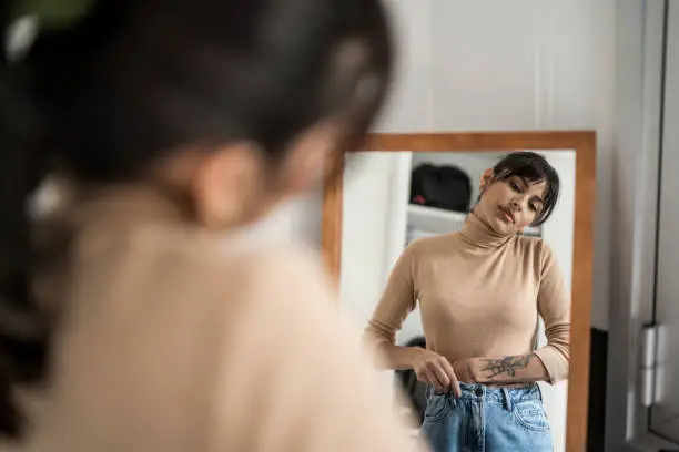 Photo of Young woman getting dressed in front of a mirror at home