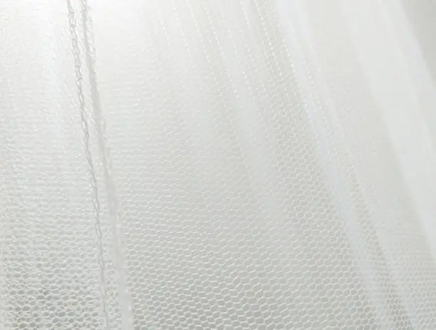 Close up of white mosquito net fabric with folds. Wavy chiffon background. Crumpled white cloth material texture. Abstract white net fabric pattern for patterns and designs.