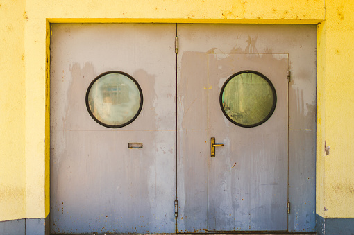 Old gray industrial door with round windows and yellow wall
