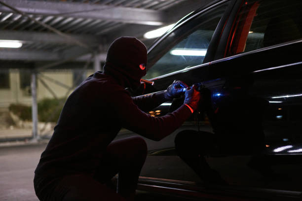 istock Focused disguised car thief, trying to break in while using the flashlight and screwdriver 1305638472