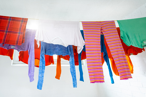 Freshly washed colored laundry in the white painted drying room of the family house hanging on the clothesline to dry. the sun shines through the window