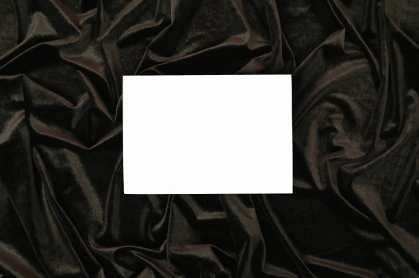 istock White invitation card mockup on a dark wavy velvet fabric. Flat lay 1305641101