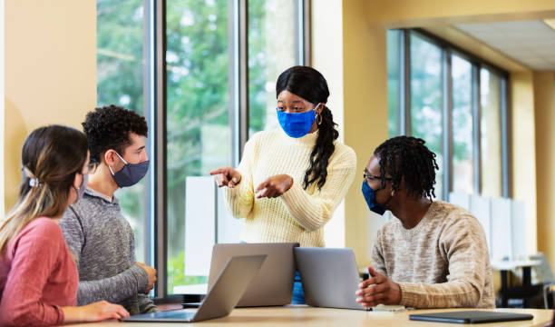 istock Young adults working together on laptops, wearing masks 1305641144