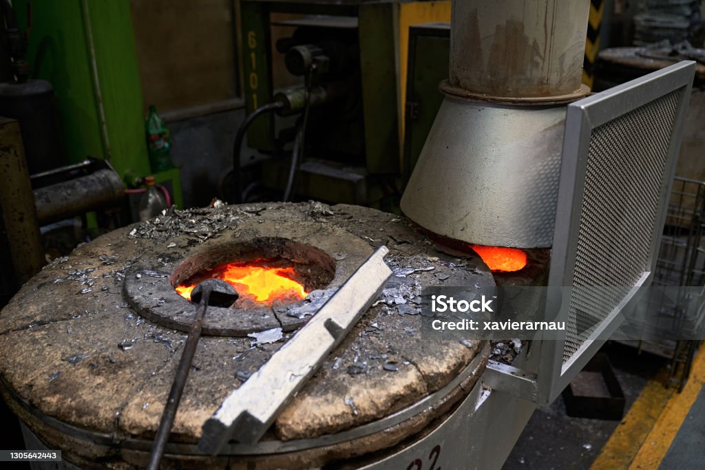 Crucible Furnace in Foundry Partial view of well-worn crucible furnace filled with molten metal and ladle. Aluminum Stock Photo