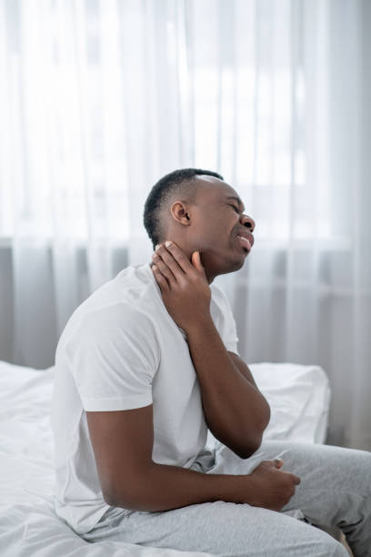 istock African american man sitting on bed and touching his neck 1305646158